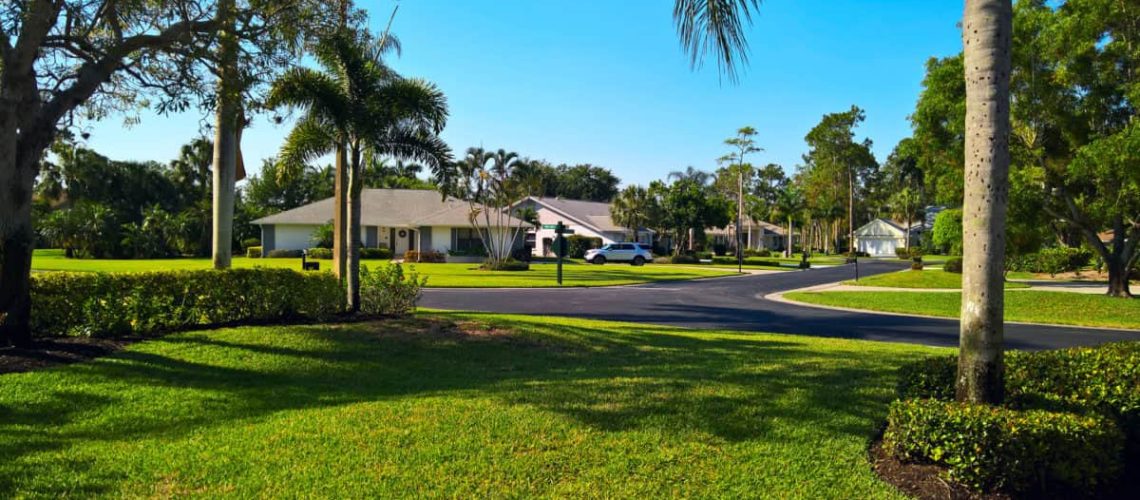 View of the golf resort with family houses, lawn and palm trees along the road under blue sky in Naples, Florida, USA